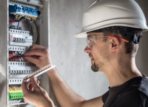 Man, an electrical technician working in a switchboard with fuses. Installation and connection of electrical equipment. Professional with tools in hand.